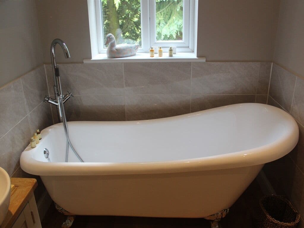 A bathroom with a freestanding bathtub, a window with a view of greenery, and a small shelf with toiletries.