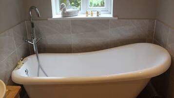 A bathroom with a freestanding bathtub, a window with a view of greenery, and a small shelf with toiletries.