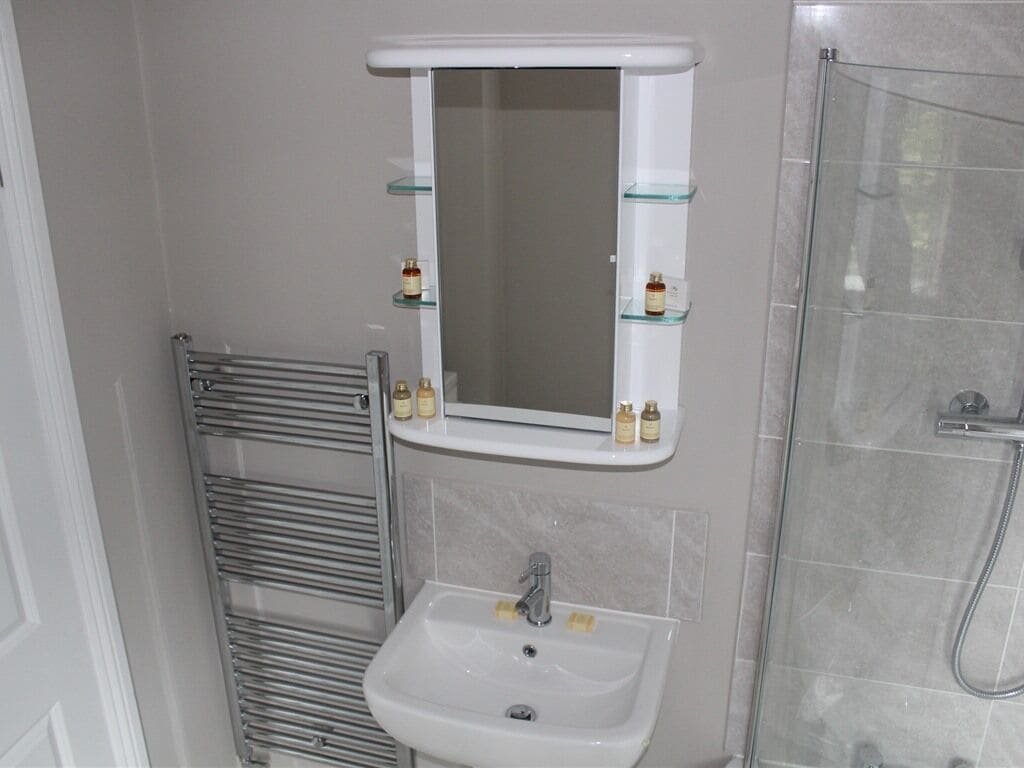 Un baño con lavamanos blanco, un espejo y cabina de ducha con mampara de vidrio.