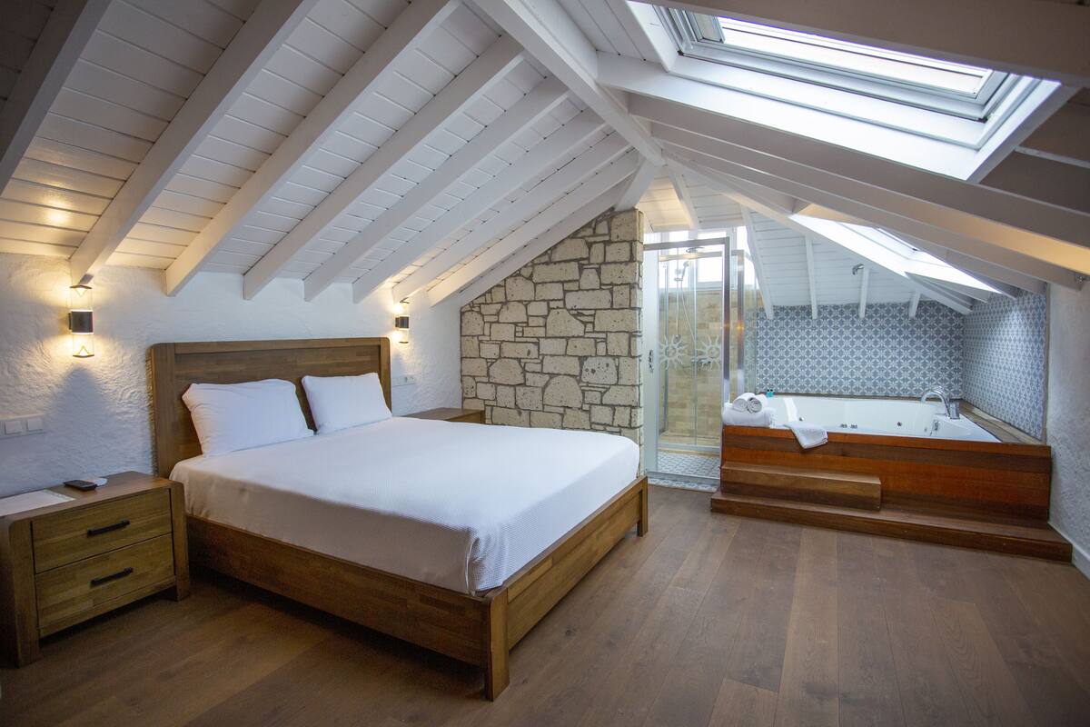 A bedroom with a wooden bed, a nightstand, a stone wall, a glass shower enclosure, and a skylight.