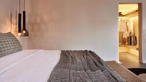 A modern bedroom with a large bed, hanging pendant lights, and a view into a bathroom with a mirror and clothes rack. - Incognito Villa (Santorini)