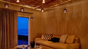 A cozy living room with a sofa, a small round table with a vase and glasses, and hanging pendant lights. - Incognito Villa (Santorini)