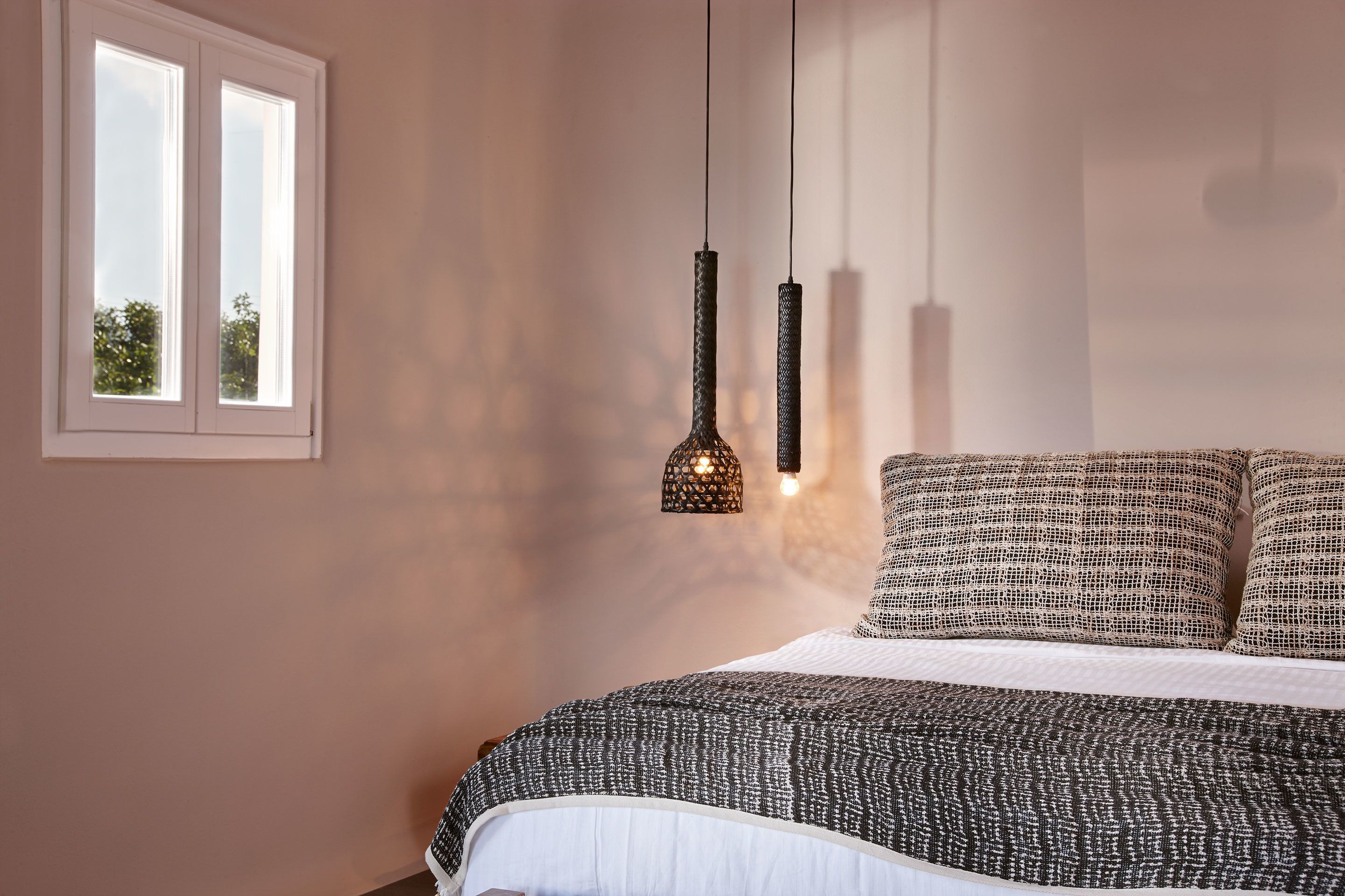 A bedroom with a large bed, a window, and two hanging pendant lights.