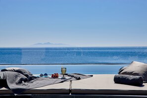 Una tumbona con vistas al mar y montañas, un vaso de agua y un plato de uvas.