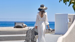 A woman in a white dress and hat walking on a terrace with a view of the sea. - Incognito Villa (Santorini)