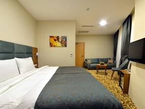 A hotel room with a large bed, a sofa, a TV, and a painting on the wall.