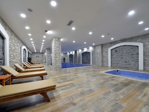 A spa area with stone walls, wooden loungers, and a pool.