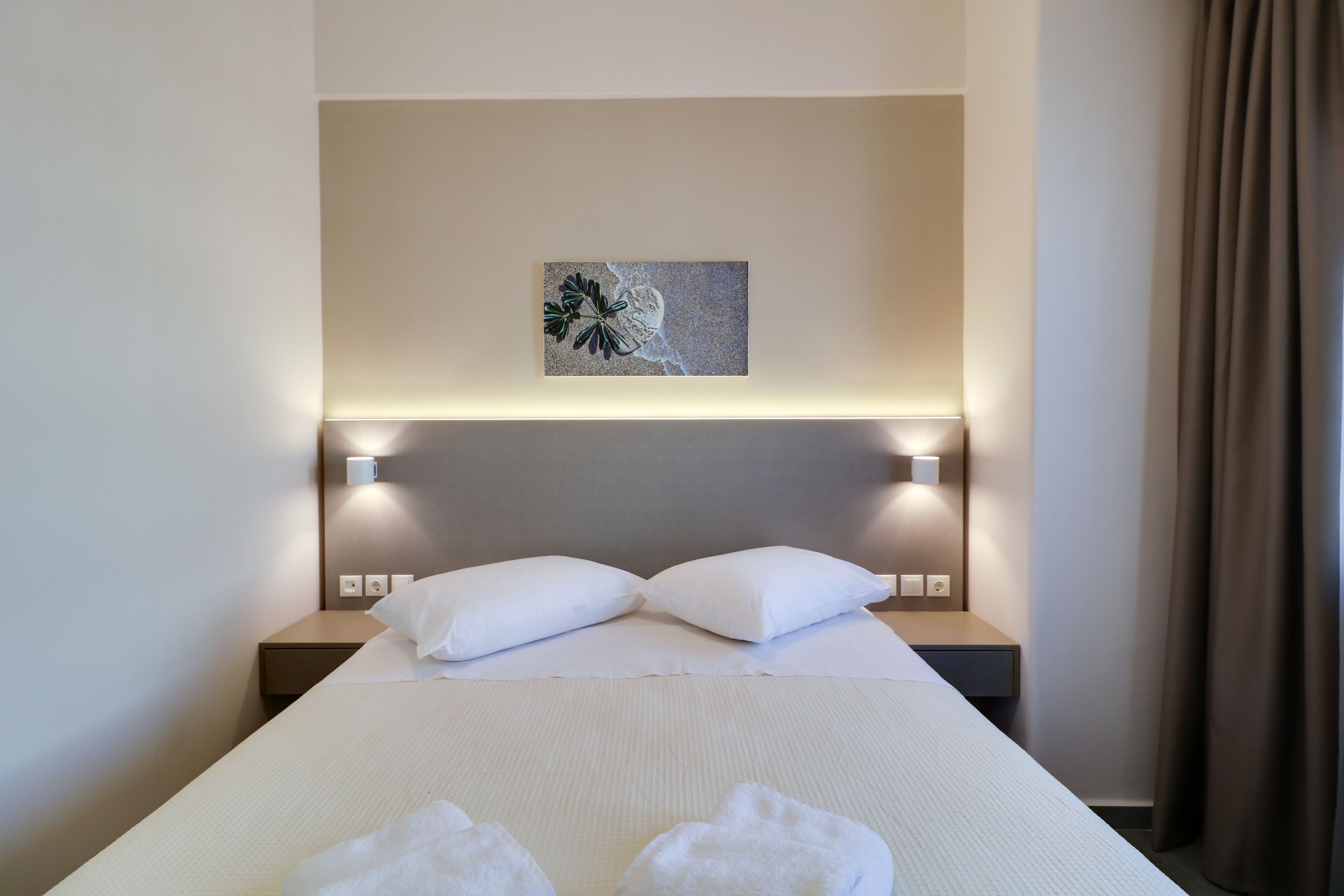 A hotel room with a neatly made bed, two bedside lamps, a wall-mounted artwork, and a window with curtains.