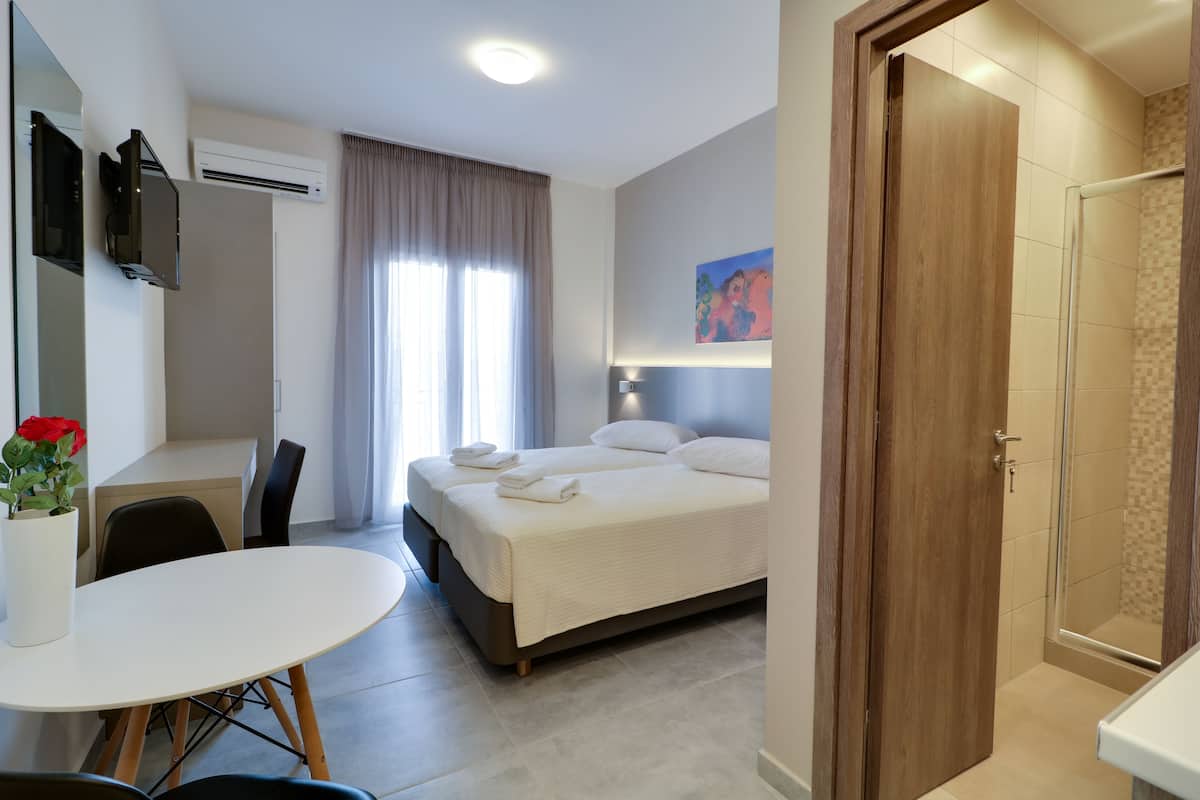 Una habitación de hotel con cama, escritorio, silla, mesa y zona de ducha.
