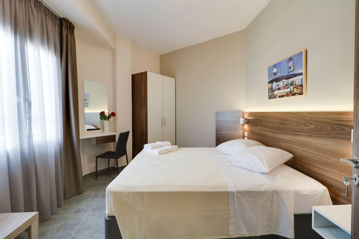 Una habitación de hotel con cama, escritorio, silla, armario y un cuadro en la pared.