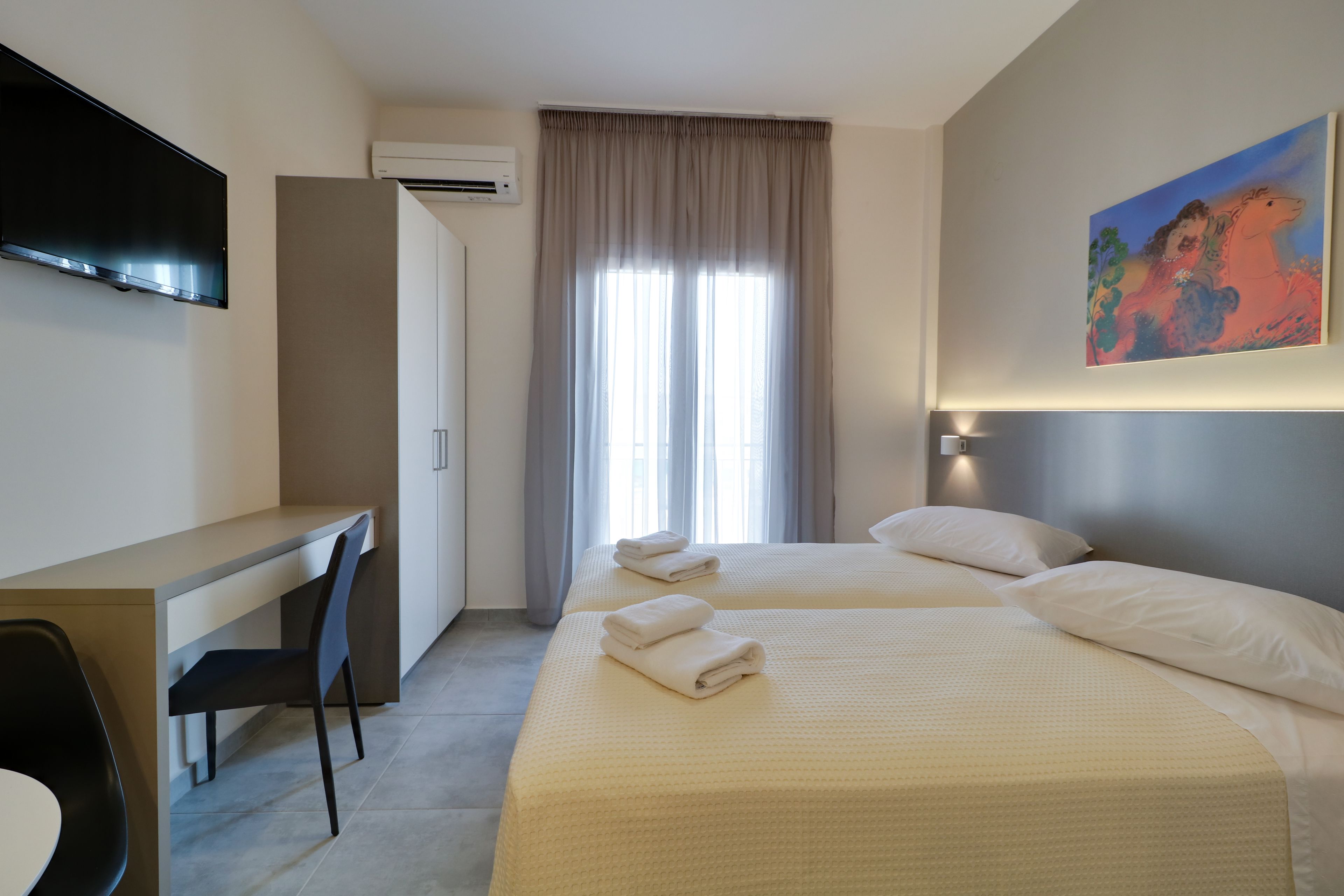 A hotel room with two beds, a desk, a chair, and a TV.