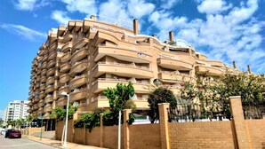 A multi-story residential building with a curved facade, balconies, and a brick wall with greenery. - Acv - costa marina I-1 línea planta 5 sur (Oropesa del Mar)