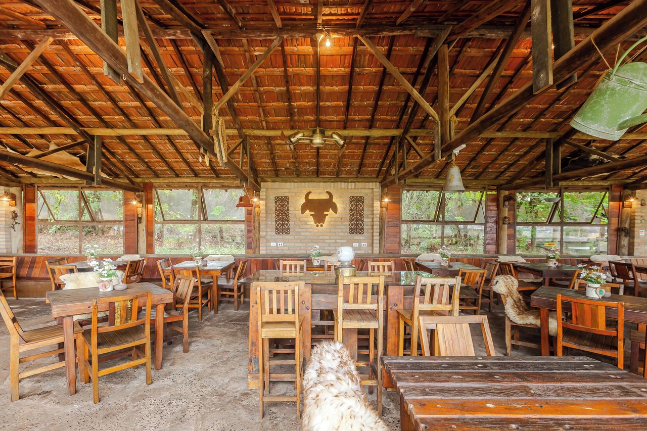 Un comedor rústico de madera con mesas y sillas, un mural de un toro en la pared y amplias ventanas que dejan entrar luz natural.