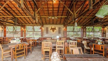 Un comedor rústico de madera con mesas y sillas, un mural de un toro en la pared y amplias ventanas que dejan entrar luz natural.