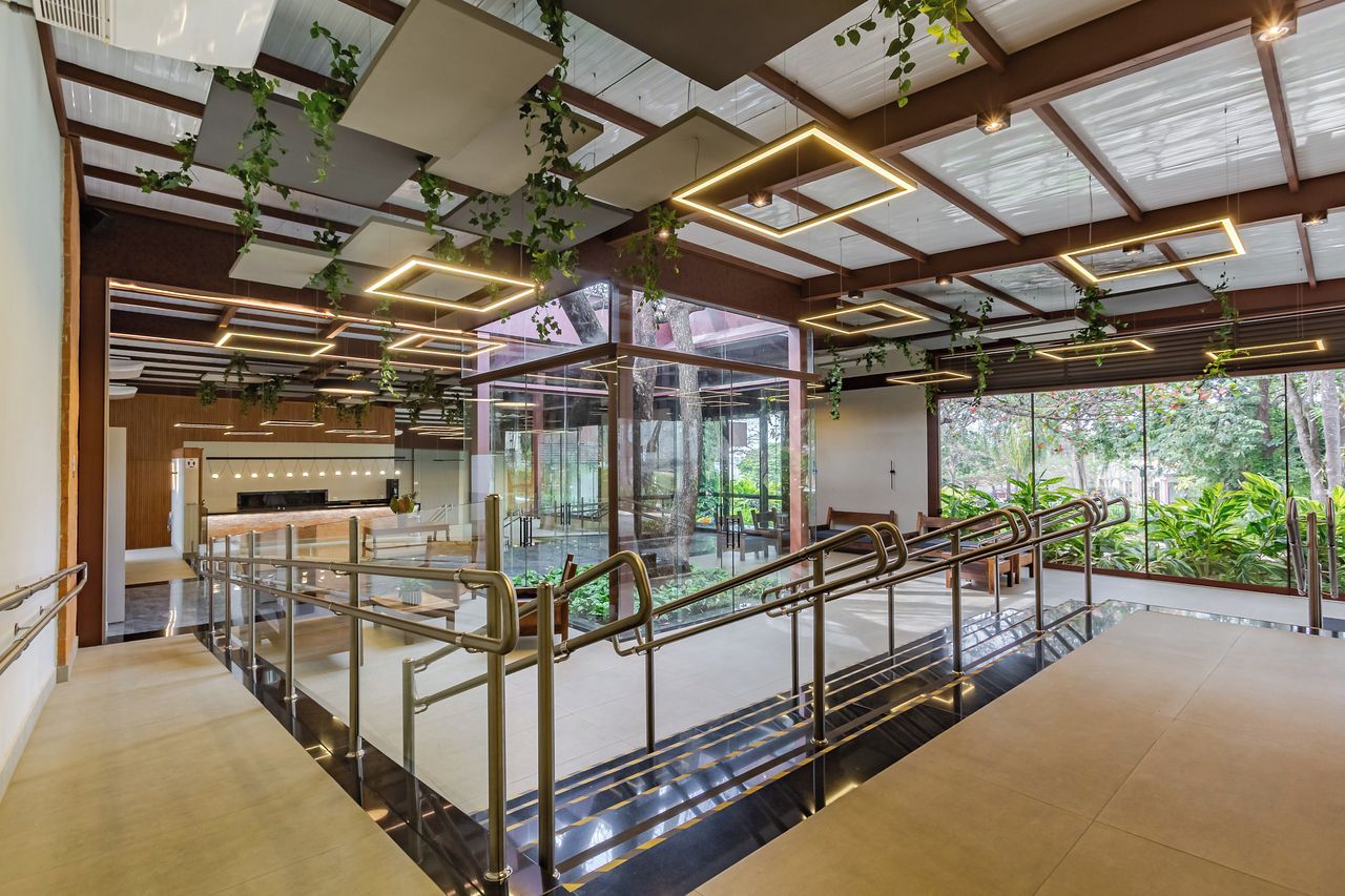 Un interior moderno con escalera de cristal, vigas de madera y plantas colgantes.