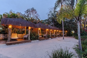 Un complexe hôtelier en bord de mer, doté de bâtiments à toits de chaume, d’espaces de détente en plein air et d’une végétation tropicale luxuriante.