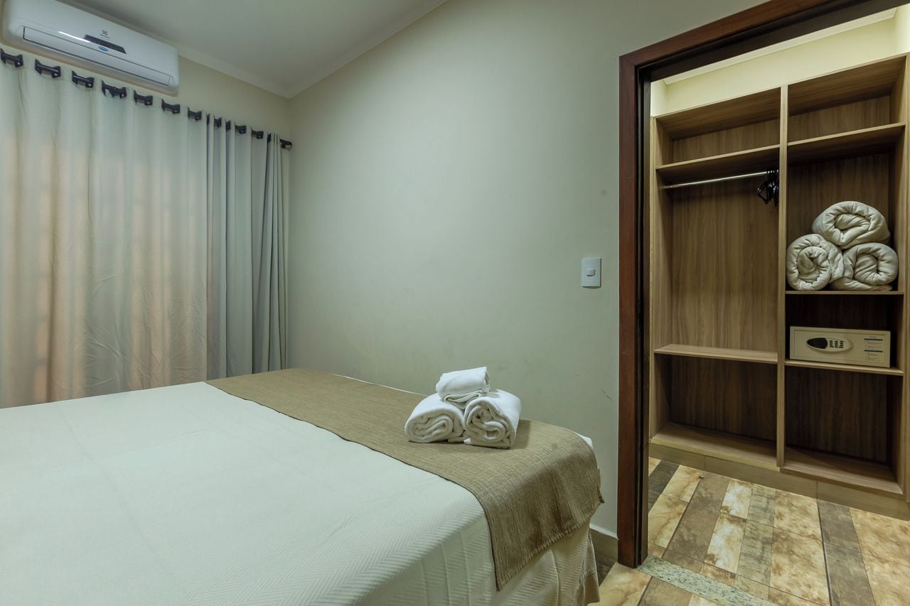 Quarto de hotel com cama, guarda-roupa e toalha dobrada sobre a cama.
