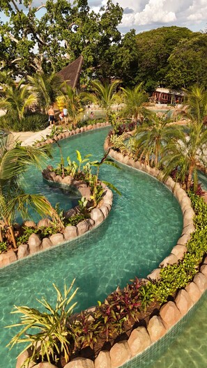Une piscine au design sinueux, entourée de plantes tropicales et de rochers.