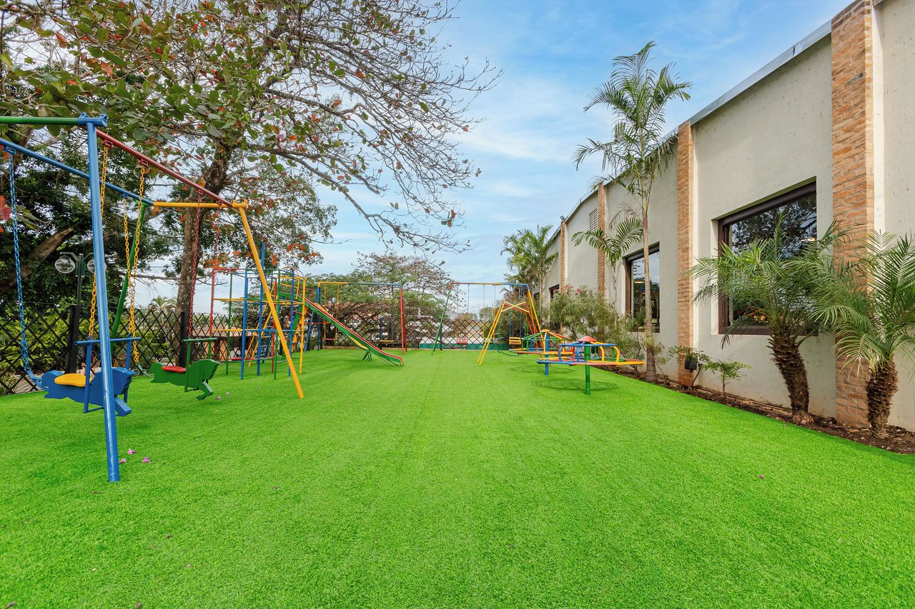 A playground with swings and slides, surrounded by a well-maintained lawn and a building with large windows.