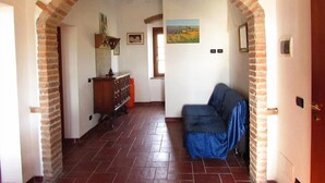 An interior space with a brick archway leading to a room with a tiled floor, a blue sofa, and a wooden cabinet.
