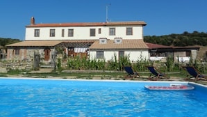 A two-story building with a swimming pool, lounge chairs, and a stone wall.