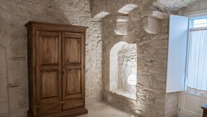 A room with stone walls, a wooden wardrobe, a window with a view, and a tiled floor. - GRAFFITI LIVING-SANTA RITA (Corato)