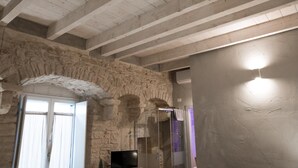 A room with stone walls, a wooden ceiling, a shower, and a flat-screen TV. - GRAFFITI LIVING-SANTA RITA (Corato)