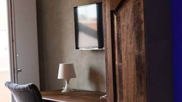 Un bureau en bois, une chaise, une lampe et un téléviseur fixé au mur.