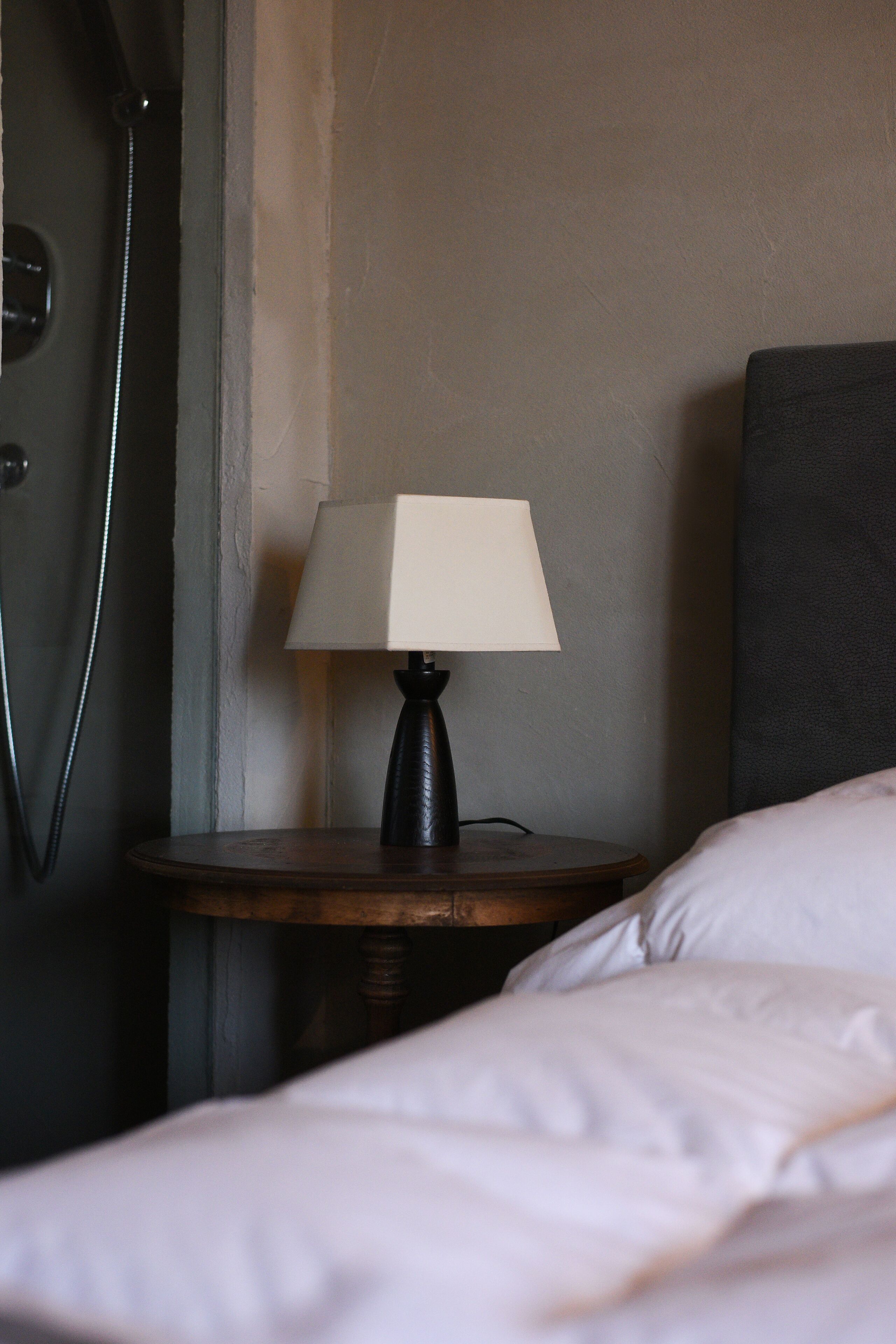 Una camera d'albergo con un letto, un comodino con una lampada e uno spazio doccia.