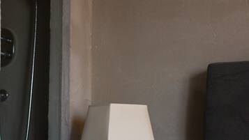Una camera d'albergo con un letto, un comodino con una lampada e uno spazio doccia.