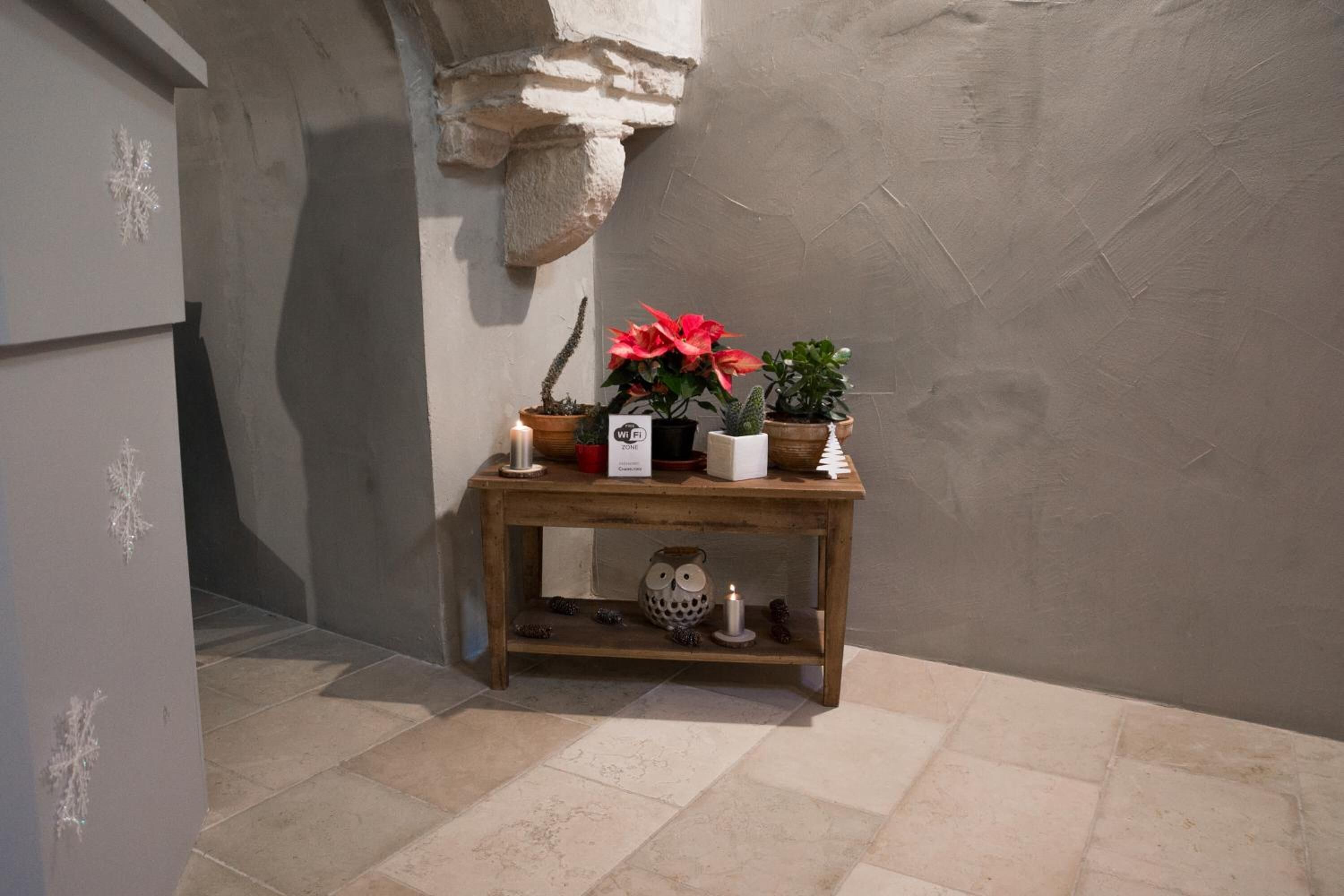 A small wooden table with potted plants and a candle, set against a plain wall with a stone feature.