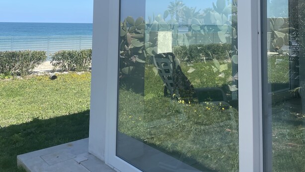 A modern building with large glass sliding doors, a white exterior, and a view of the ocean. - GRAFFITI LIVING-SANTA RITA (Corato)