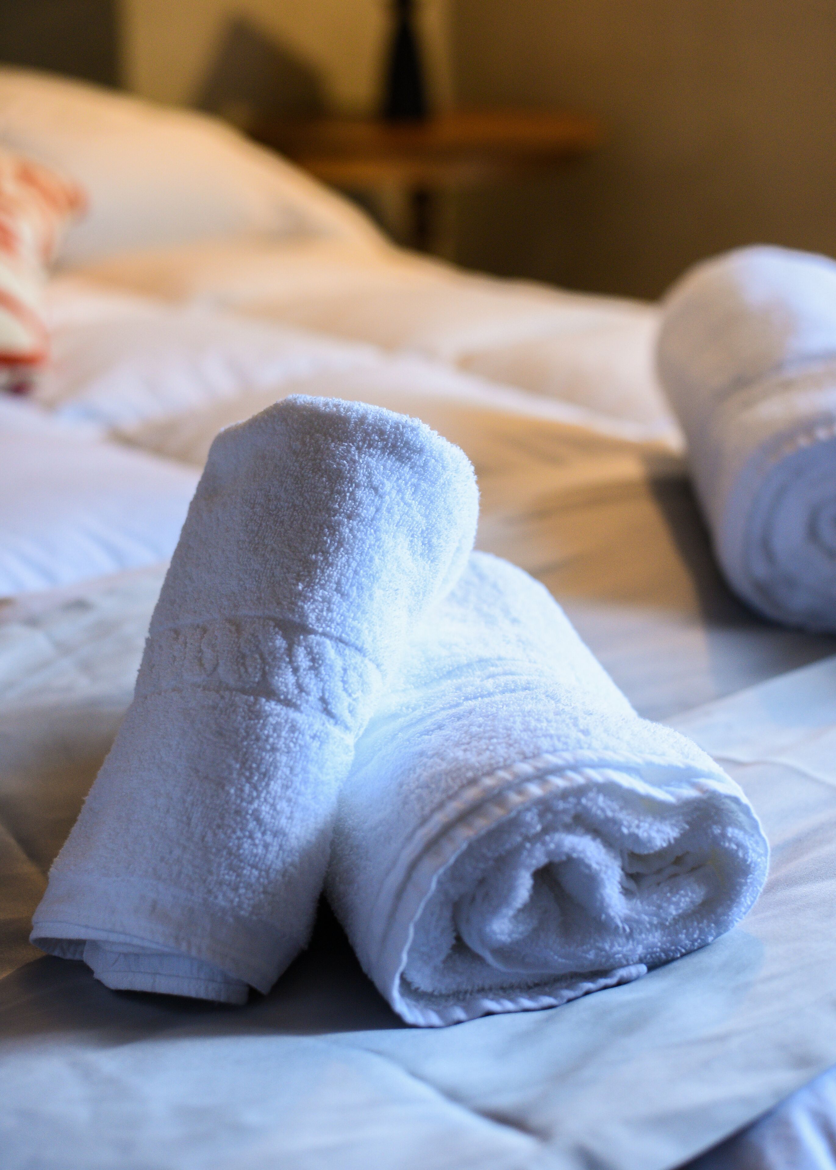 A neatly made bed with white linens and rolled towels.