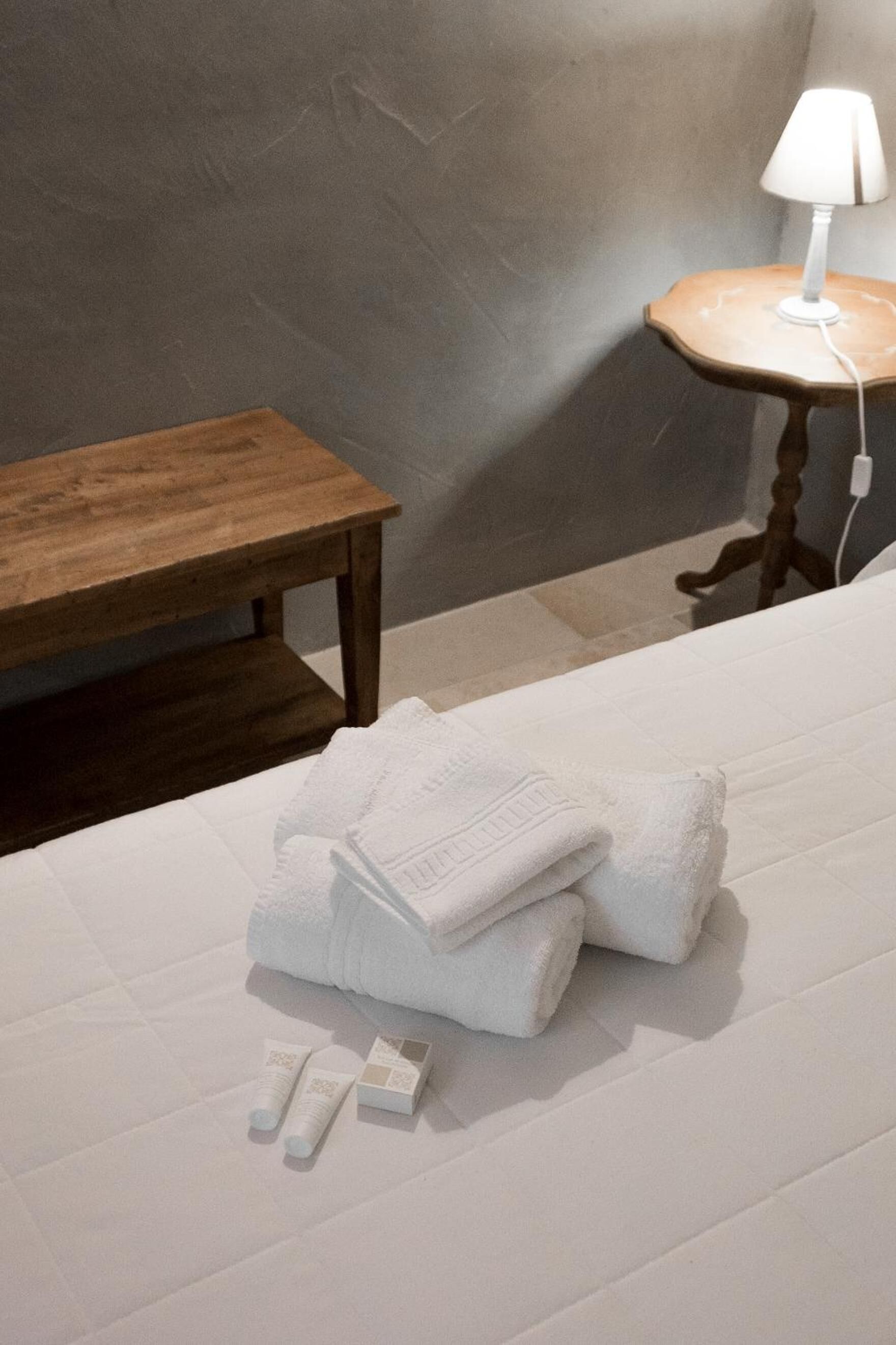 A neatly made bed with folded white towels and toiletries on a white bedspread.
