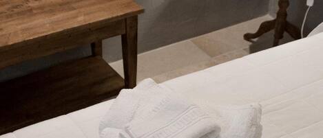 A neatly made bed with folded white towels and toiletries on a white bedspread.