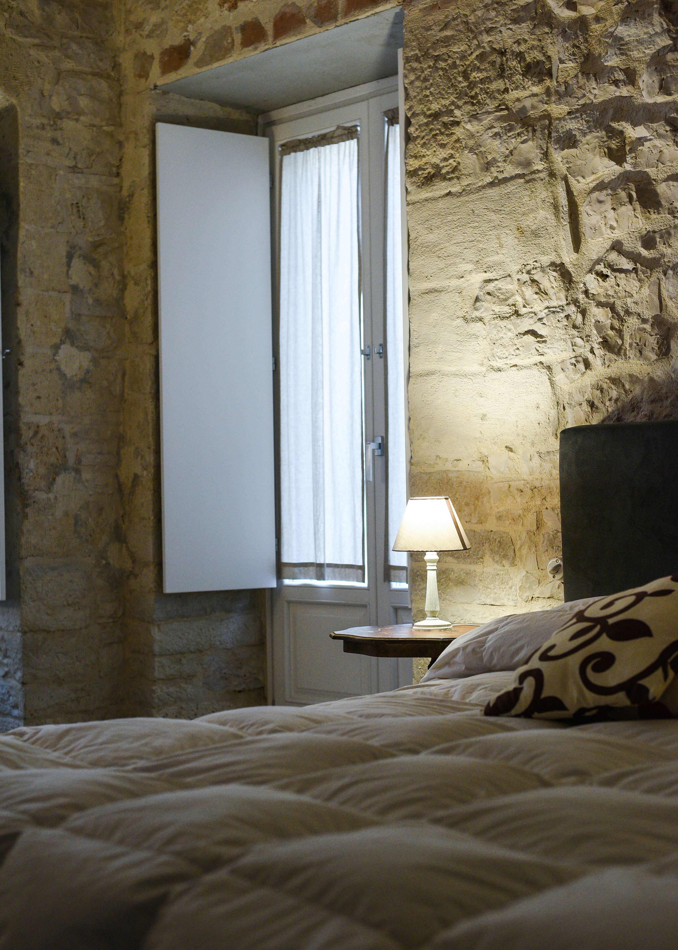 A bedroom with a bed, a nightstand, a lamp, and a window with curtains.