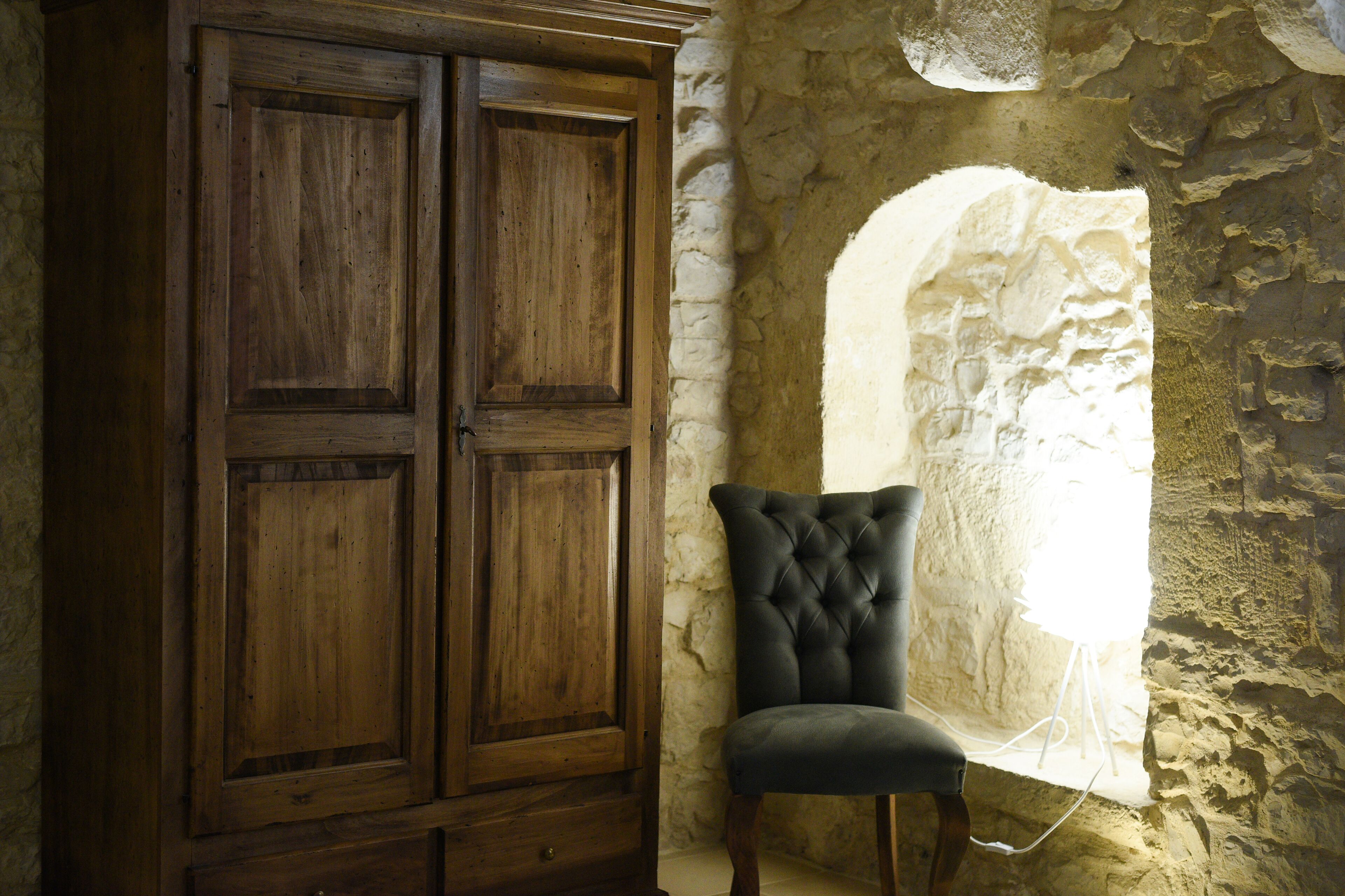 Un armario de madera, un sillón acolchado y una pared de piedra con una ventana.