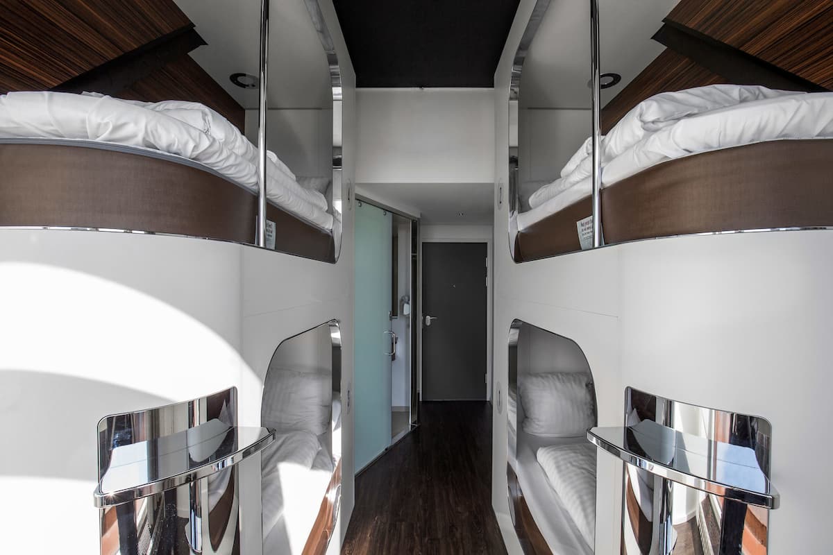 A narrow, modern hotel room with bunk beds and a small table.