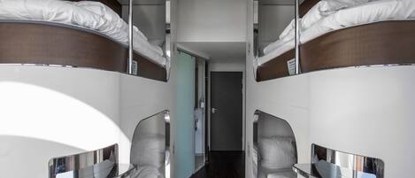 Quarto de hotel moderno e estreito, com beliches e uma mesa pequena.