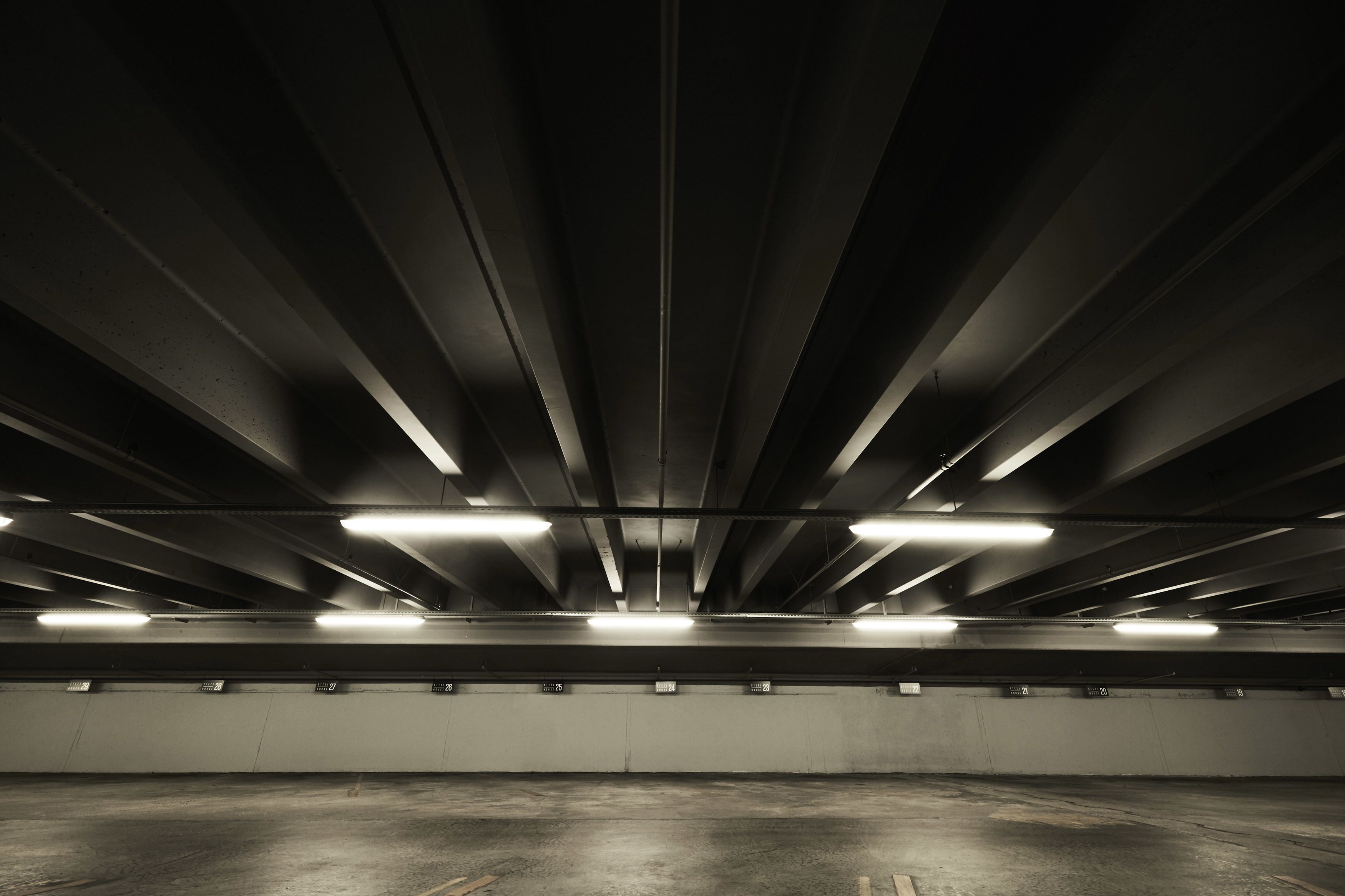 A parking garage with multiple levels and rows of parking spaces, illuminated by overhead fluorescent lights.