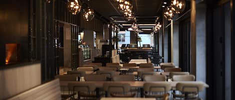 A restaurant with long tables and chairs, hanging pendant lights, and a view of the street outside.