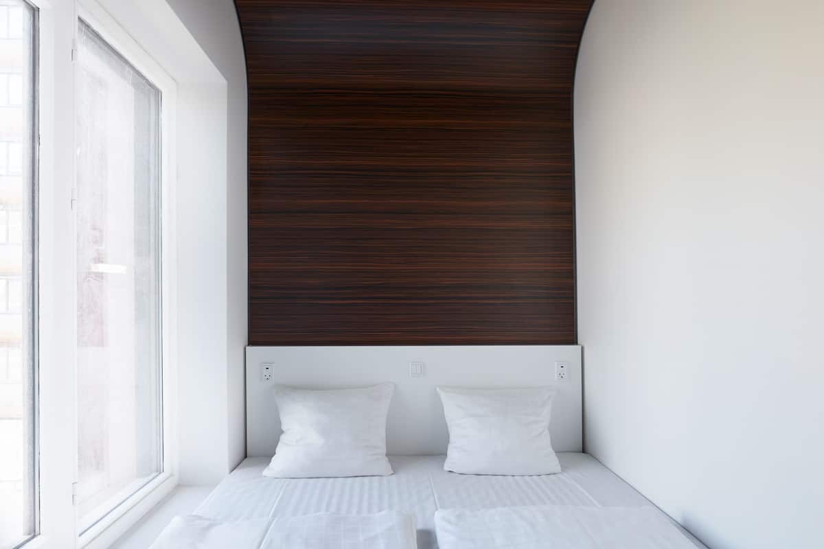 A modern room with a white bed, two white pillows, and a dark wooden ceiling.