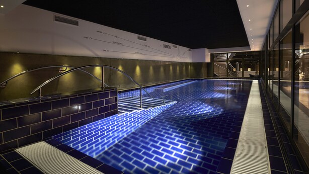 Une piscine intérieure moderne, avec des marches recouvertes de carreaux bleus et un plafond sombre.