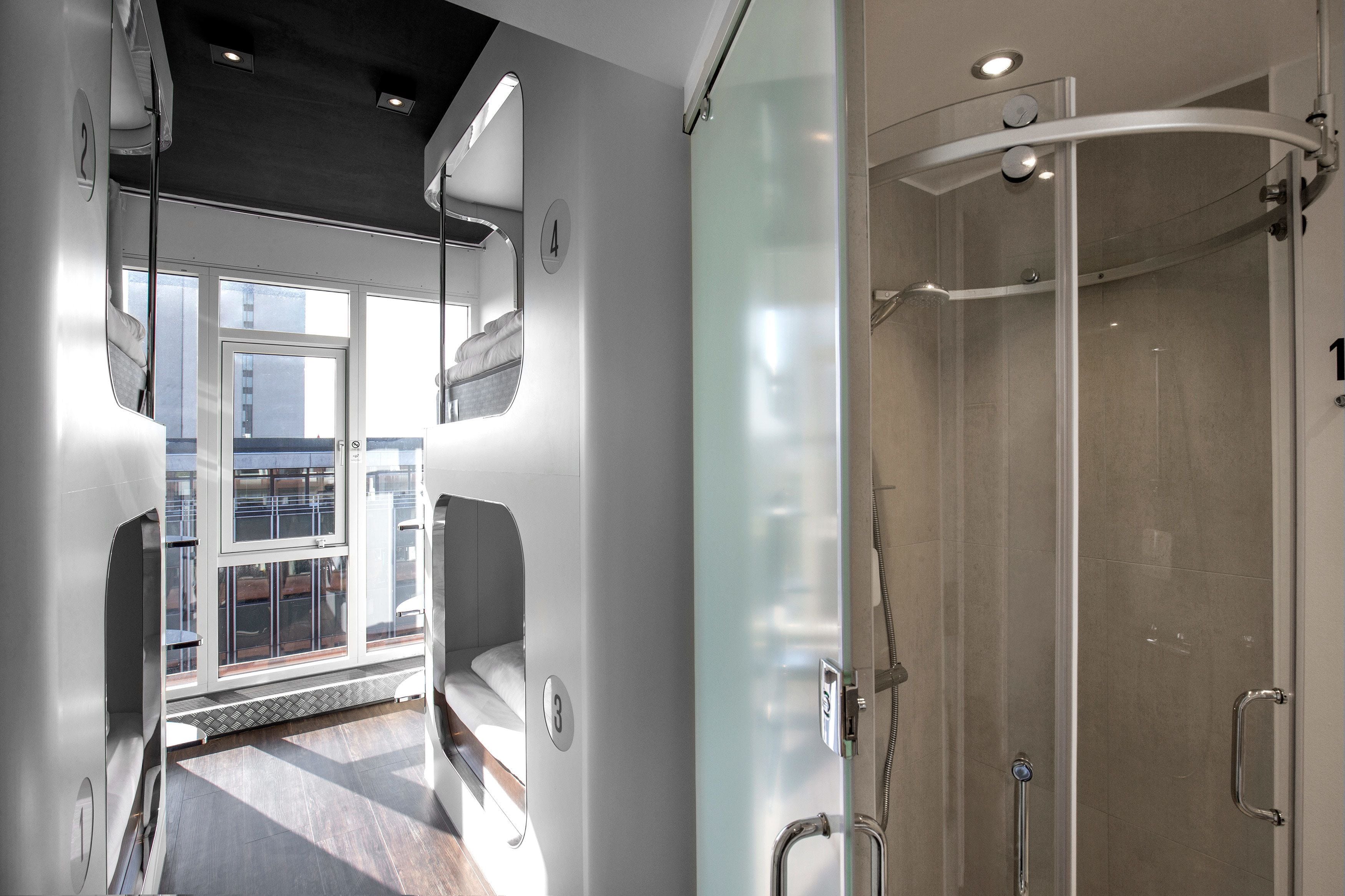 Une salle de bain moderne avec une douche à l’italienne en verre, une fenêtre visible et un lit offrant une belle vue.