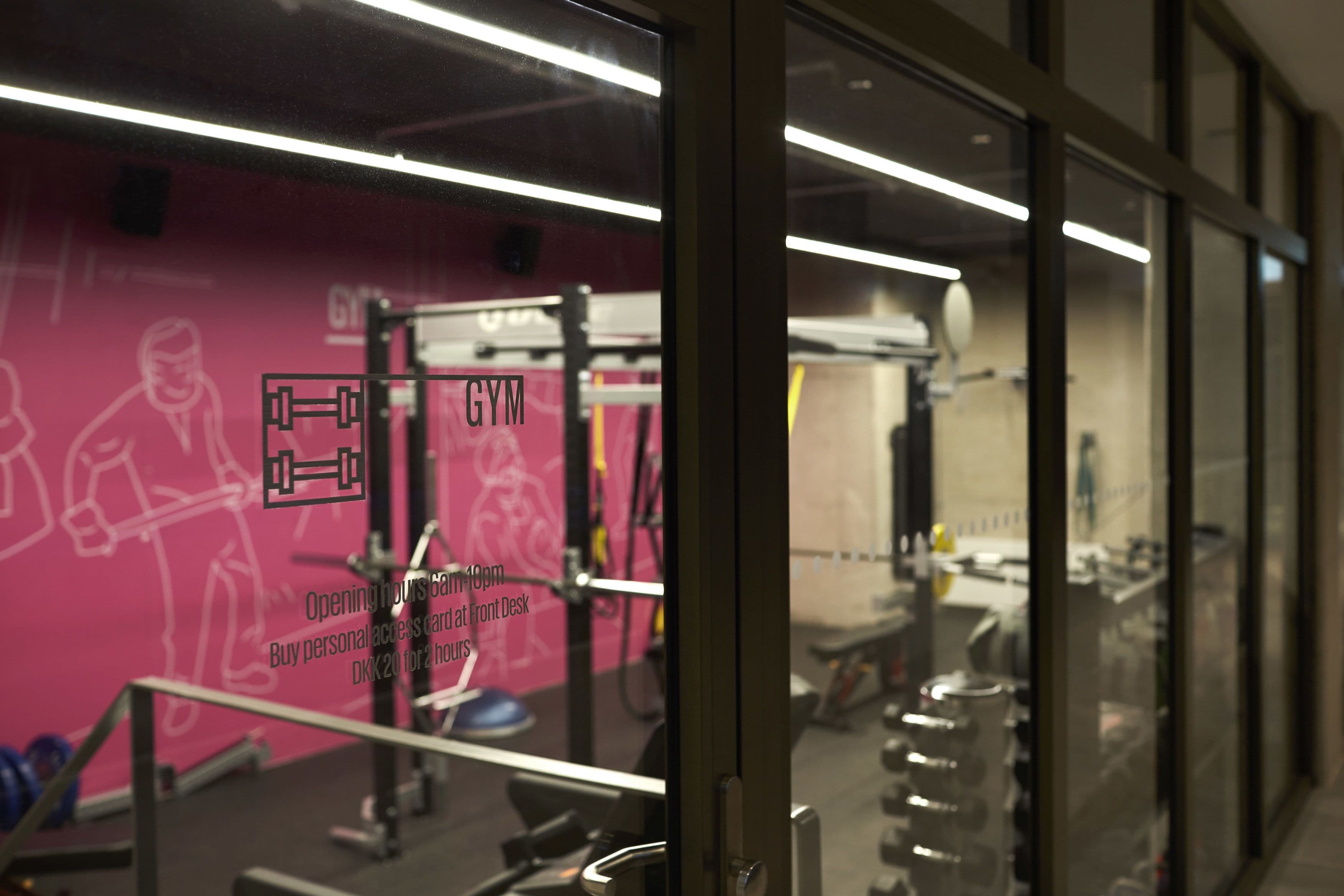 Una palestra con attrezzature per esercizi, uno specchio a parete e una parete rosa con illustrazioni a tema fitness.