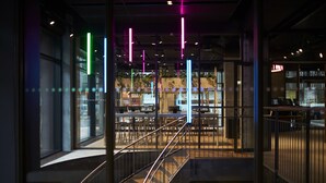 Un intérieur moderne avec un escalier, des murs en verre et des luminaires verticaux aux couleurs vives.