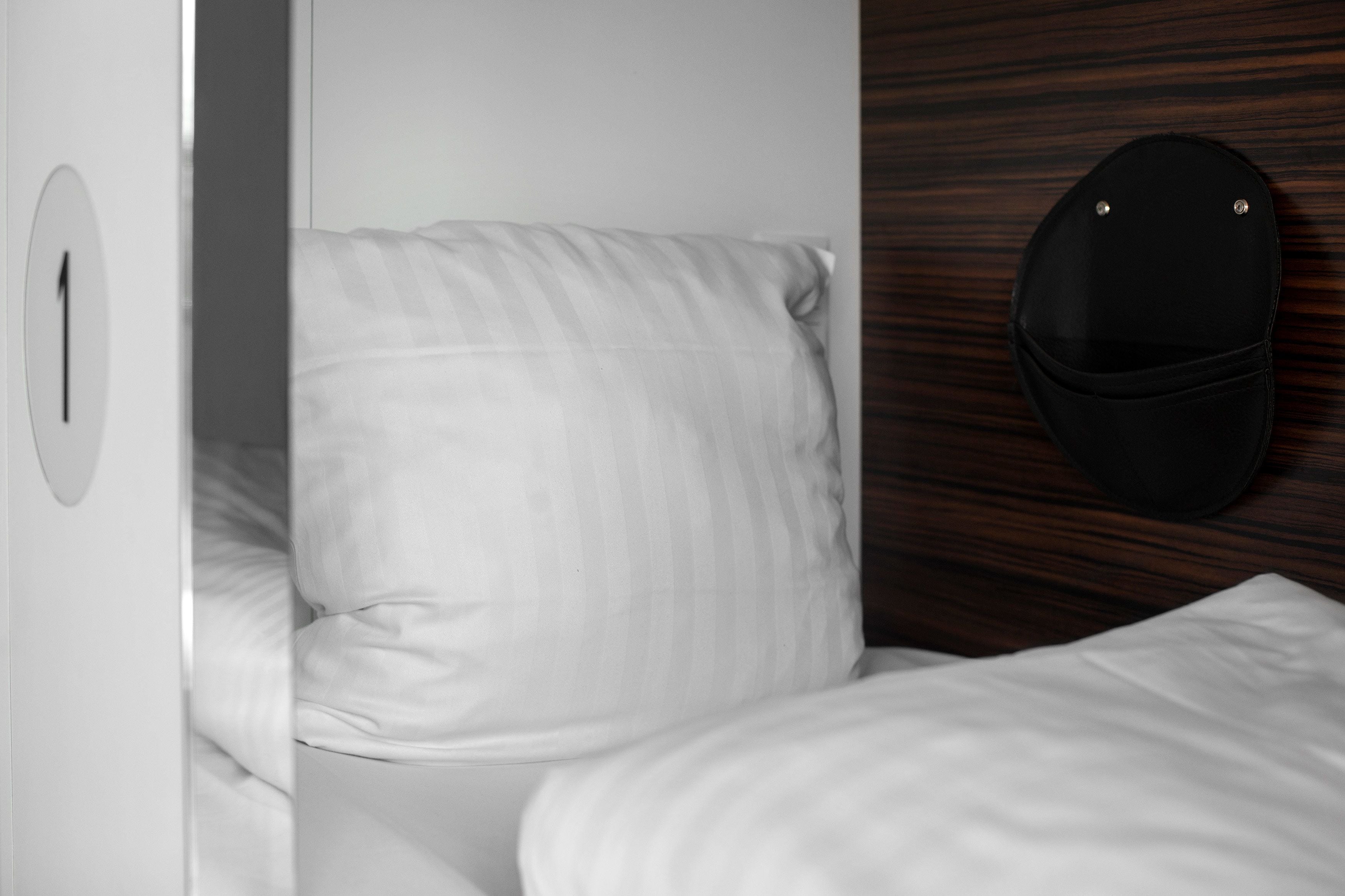 Un lit avec une literie blanche, une tête de lit en bois et un chapeau noir accroché au mur.