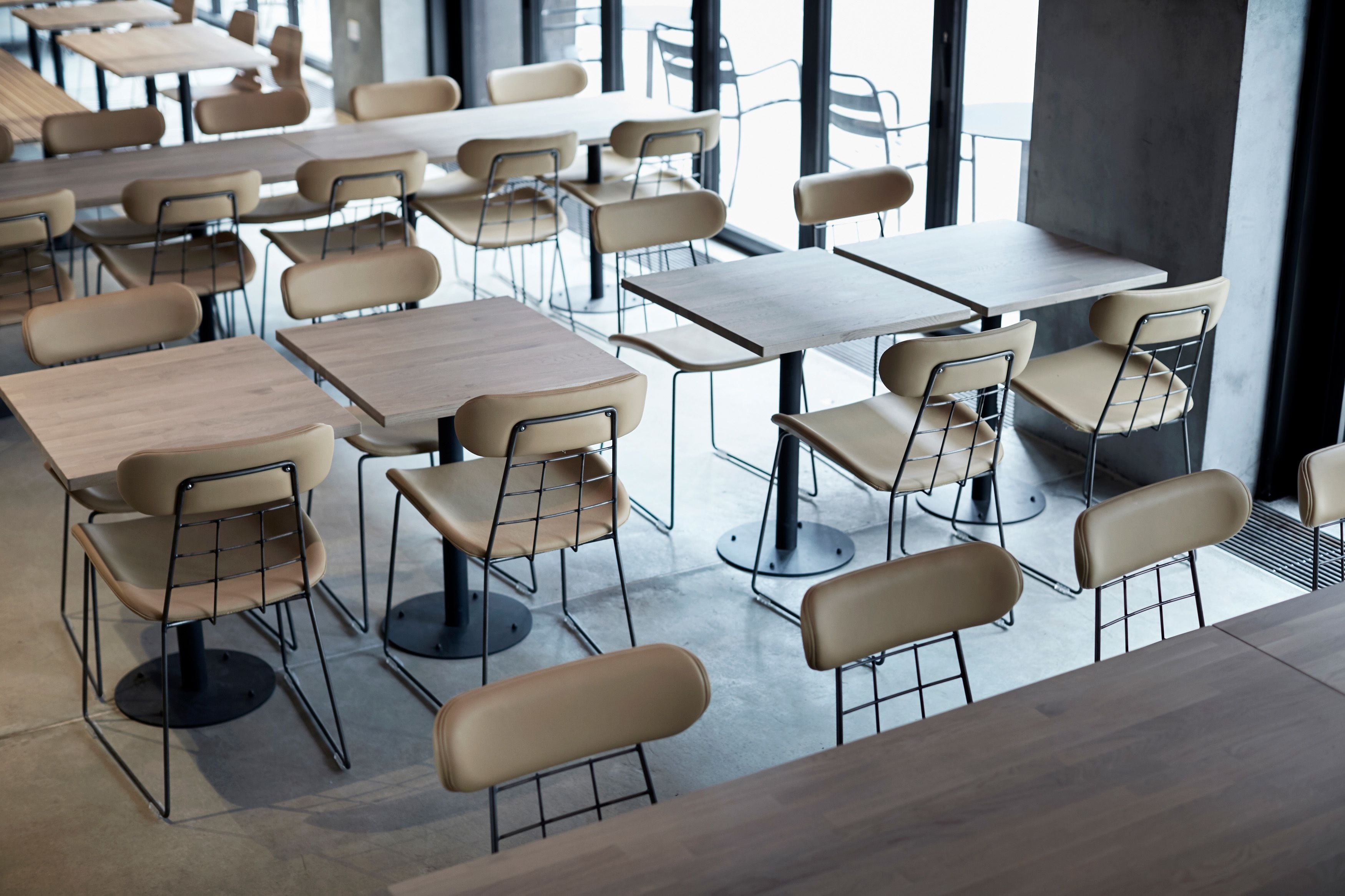 Un espace repas moderne doté de plusieurs tables et chaises, de grandes fenêtres et d’un sol en béton.