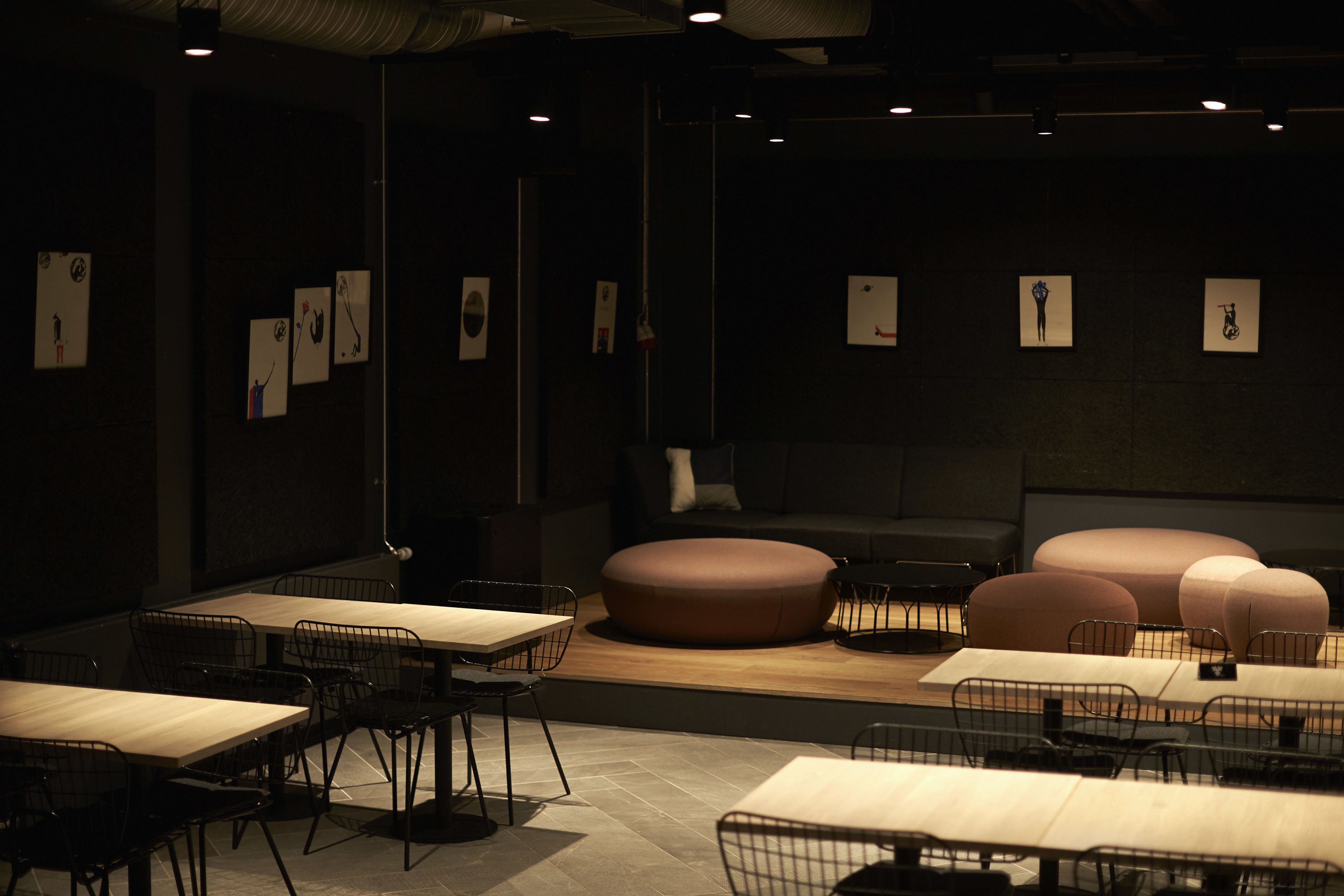 A modern interior with tables and chairs arranged for dining, a central seating area with a sofa, and artwork on the walls.