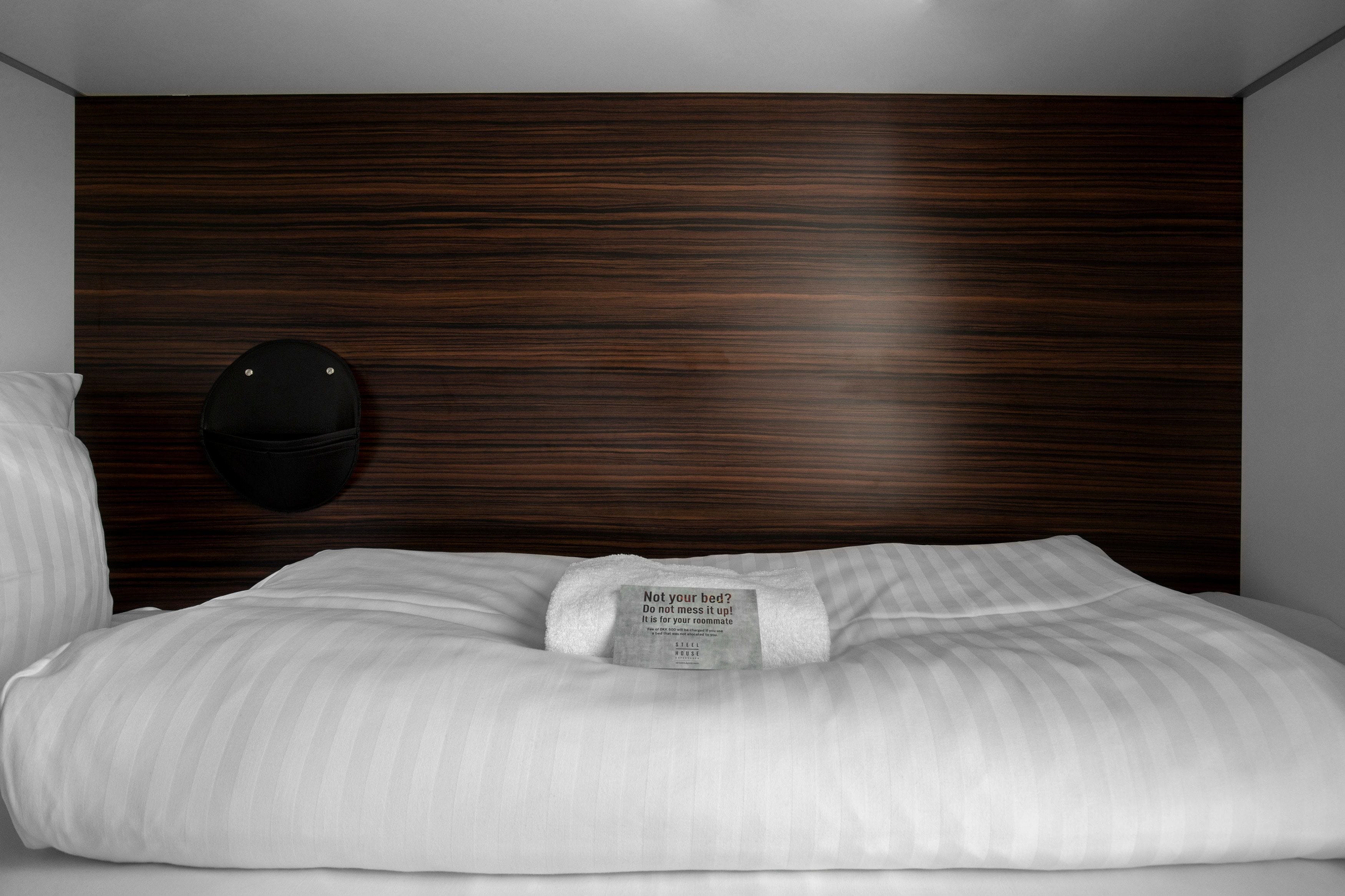 A neatly made bed with a pillow and a tag that reads "Not your bed? Do not mess it up! It is for your roommate."